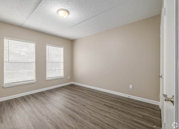 A room with wooden flooring and two windows.