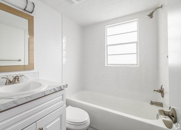 A white bathroom with a marble countertop and a large mirror.