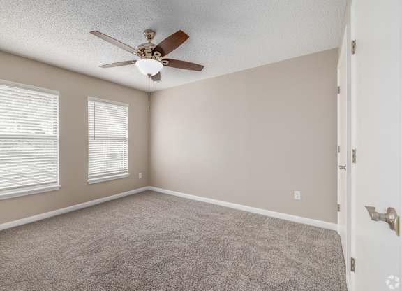 A room with a ceiling fan and two windows.