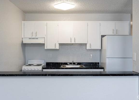 A kitchen with white cabinets and a black countertop.