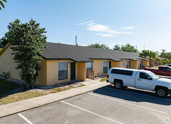 A white truck is parked in a parking lot in front of a yellow building.