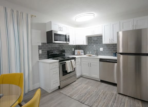 A modern kitchen with a yellow chair and a stainless steel refrigerator.