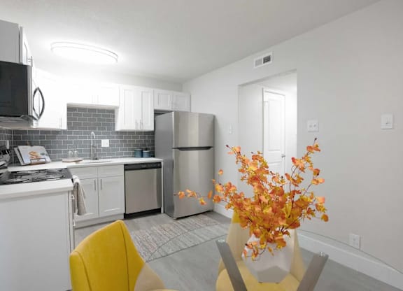 A kitchen with a yellow chair and a vase of flowers on the table.
