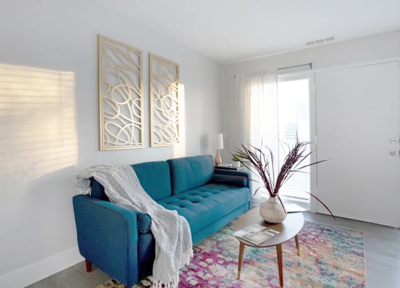 A blue couch with a white blanket on it sits in a room with a wooden coffee table in front of it.