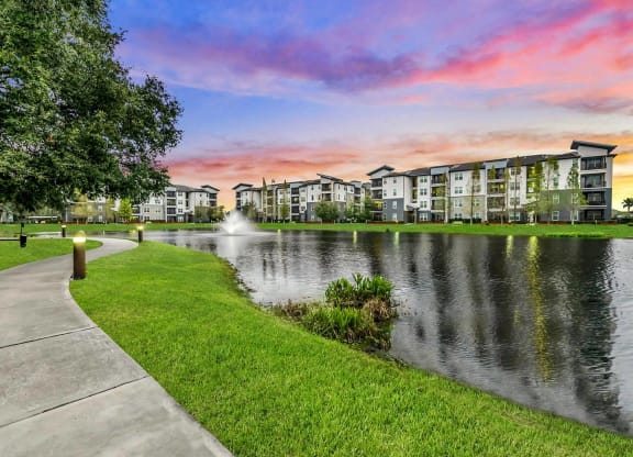 a sidewalk next to a lake with a fountain at Pearce at Pavilion Luxury Apartments, Riverview, Florida
