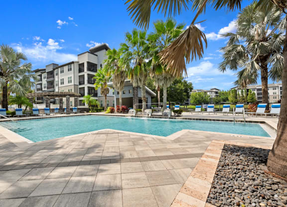 a swimming pool with palm trees and buildings in the background at Pavilion Luxury Apartments, Riverview, FL, Florida