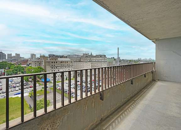 A balcony with a metal railing overlooks a parking lot and buildings.