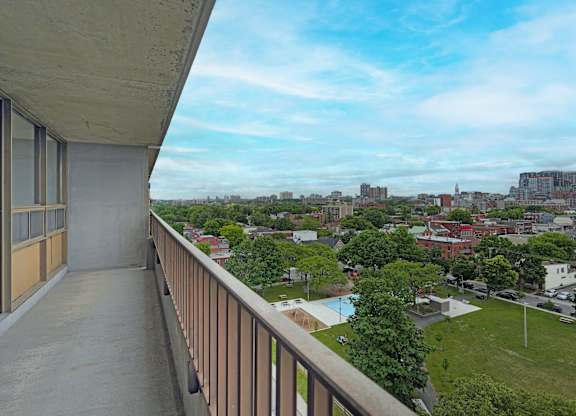 A balcony overlooks a cityscape with buildings and a pool.