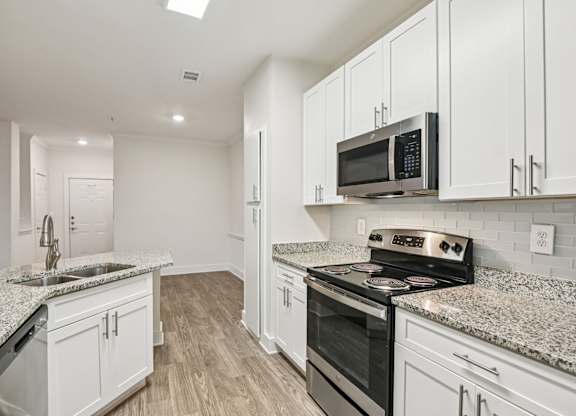 A renovated kitchen with white cabinets, granite countertops through out and stainless steel appliances