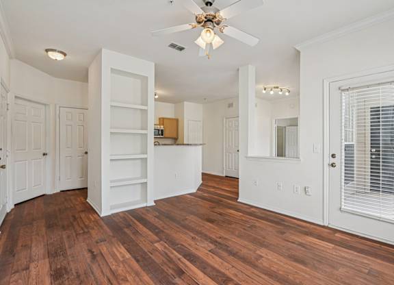 A living room with a ceiling fan, wooden floors., and a built-in bookcase.
