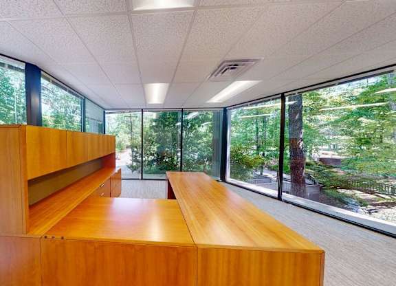 A long wooden table is in a room with a view of trees outside.
