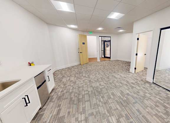 A spacious office room with a carpeted floor and white walls.