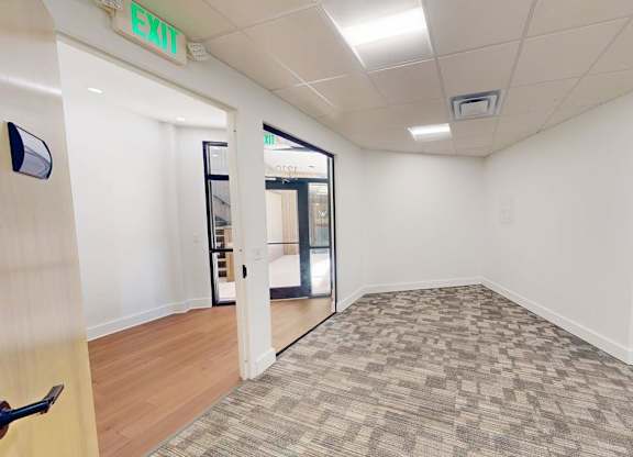 A room with a carpeted floor and a green exit sign on the wall.