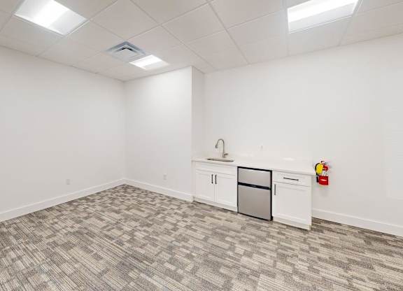 A white room with a grey carpet and a fridge.