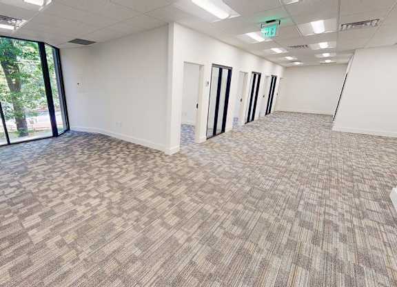 A spacious office room with carpeted flooring and large windows.