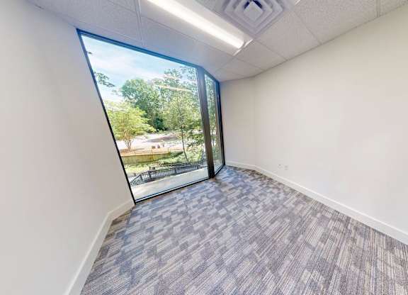 A room with a carpeted floor and a window that opens to a view of a park.