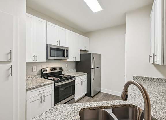 A renovated kitchen with white cabinets, granite countertops through out and stainless steel appliances