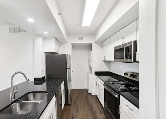 A modern kitchen with stainless steel appliances, black countertops and white cabinets.