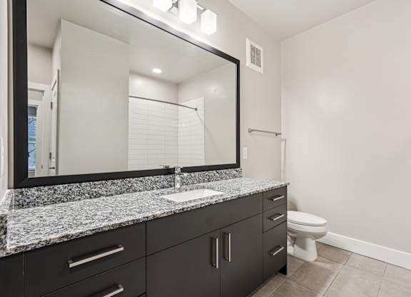 A modern bathroom with granite countertops,  a sink, mirror, and toilet.