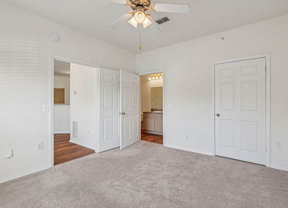 A spacious bedroom with a ceiling fan, carpeted floor and attached bathroom
