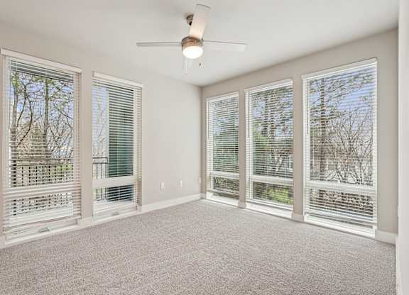 A large bedroom with floor to ceiling windows all through out the room,  a ceiling fan
