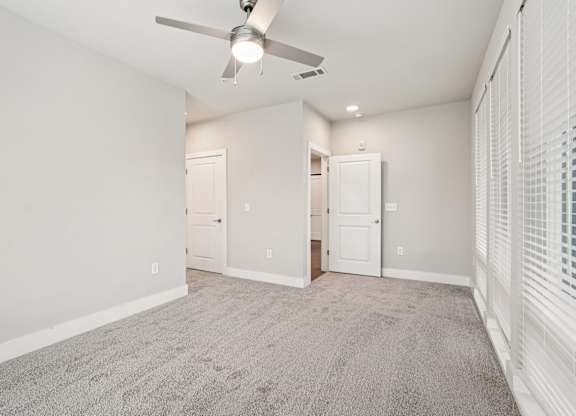 A large bedroom with floor to ceiling windows all through out the room, carpeted floor, a ceiling fan