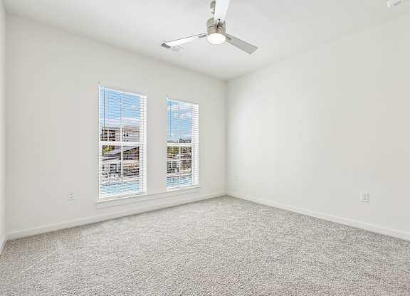 A room with a carpet floor, a ceiling fan, and two windows.