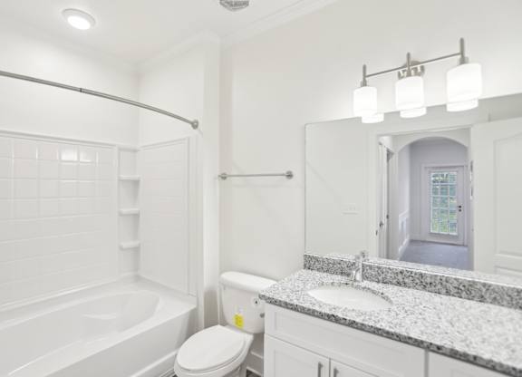 A bathroom with a tub, toilet, and granite sink.