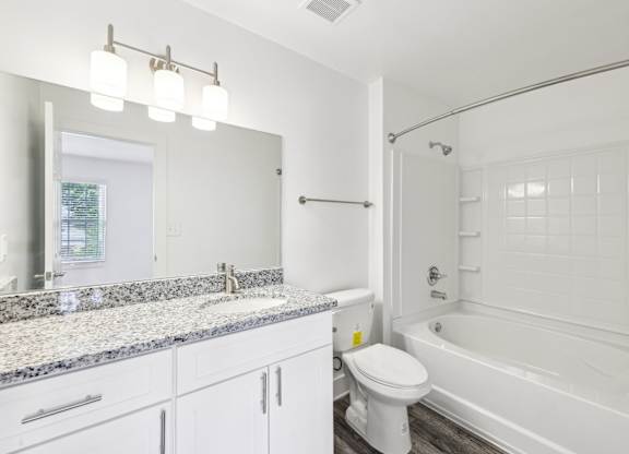 A white bathroom with a granite countertop and a white toilet.