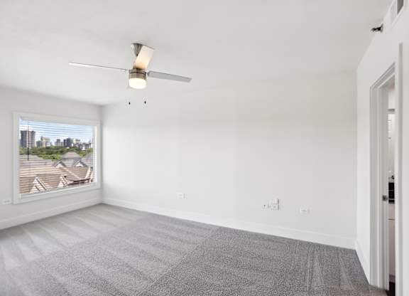 A room with a ceiling fan and a window overlooking a cityscape.