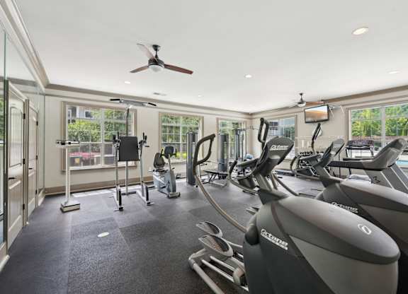 A gym with treadmills, elliptical machines, other equipment,  and a fan.