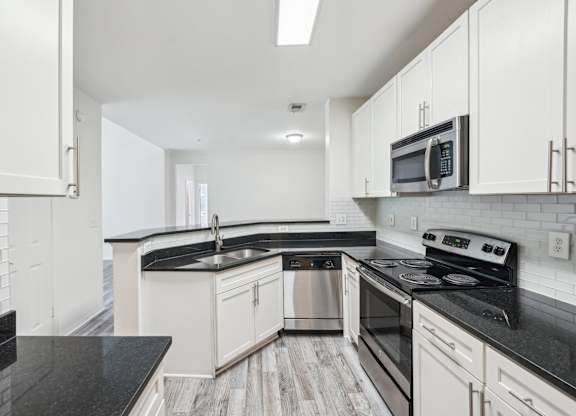 A kitchen with black countertops, stainless steel appliances, and white cabinets.