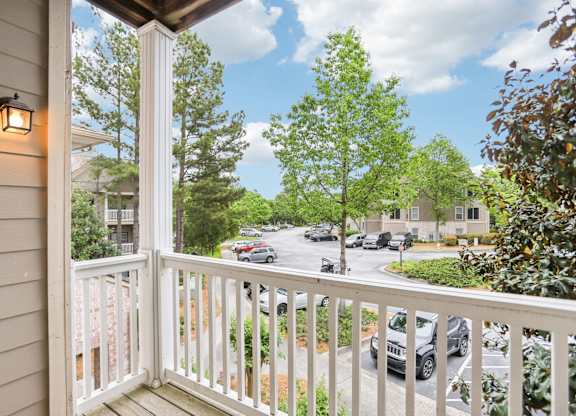 A view from a balcony overlooking a street with cars and trees.