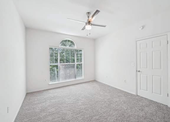 A great naturally lighted room with carpet, a ceiling fan and a window.