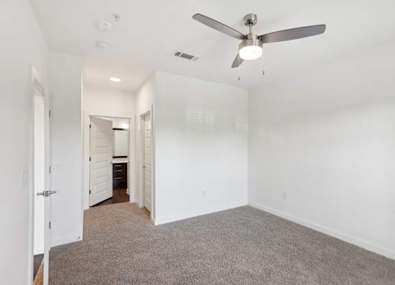 A bedroom with a ceiling fan and carpeted floor.