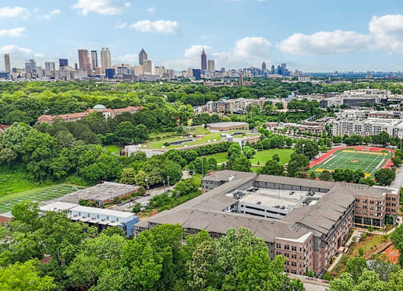 A view of a city from a high vantage point with buildings, trees, and a sports field.