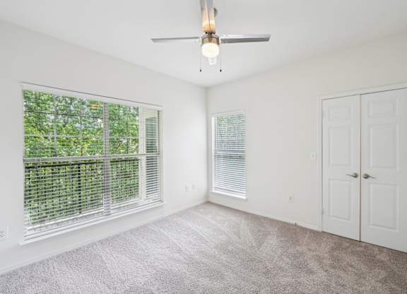 A room with a ceiling fan and two windows with blinds.