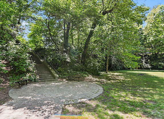 A circular stone pathway leads up a staircase in a lush green park.