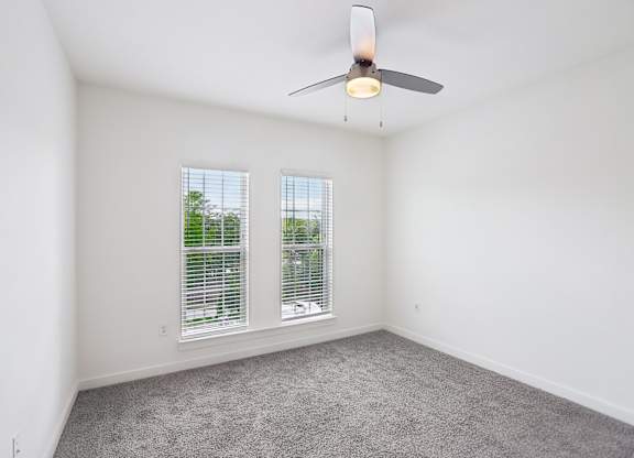 A bedroom with a ceiling fan and two windows.