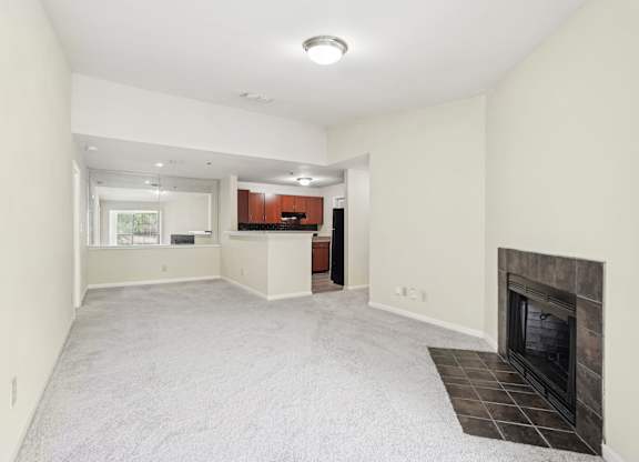 A spacious living room with a fireplace and a kitchen in the background.