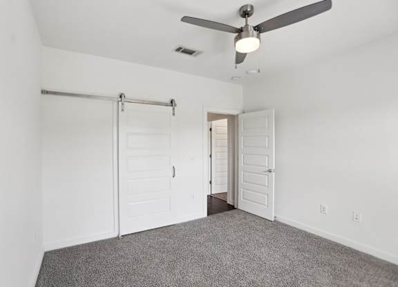 A bedroom with a ceiling fan and barn door closet.