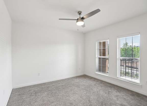 A large bedroom with a ceiling fan, windows, and carpeted floor.