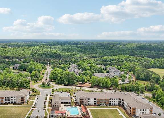 aerial view of the apartment complex with the pool ad many trees in view with beautiful skies