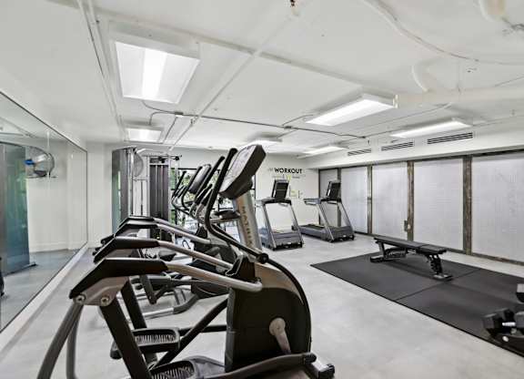 A gym with treadmills, elliptical machines, a bench, and free weights.