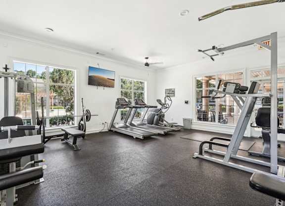 A spacious gym with various exercise equipment and a view of the outdoors through the windows.