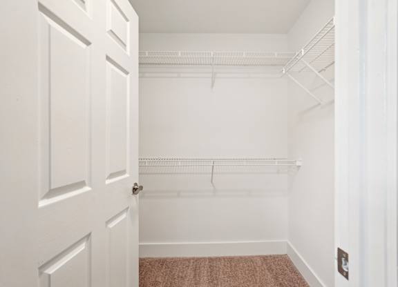 A white door is open to a room with a white wall and a brown carpet.