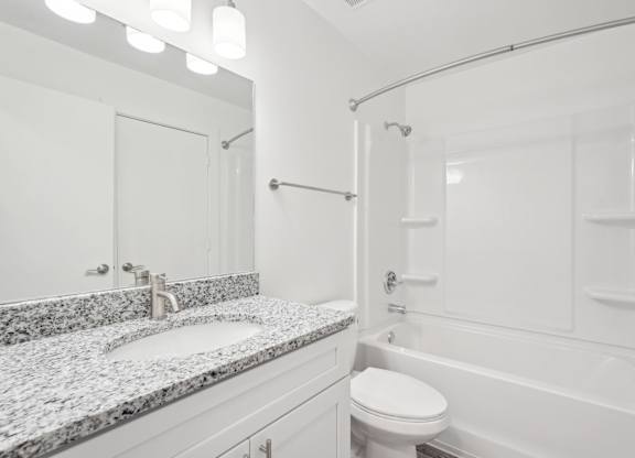 A bathroom with a granite countertop and a white tub and shower