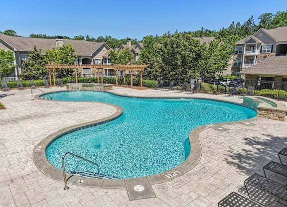 A large outdoor swimming pool surrounded by a wooden fence and residential houses.