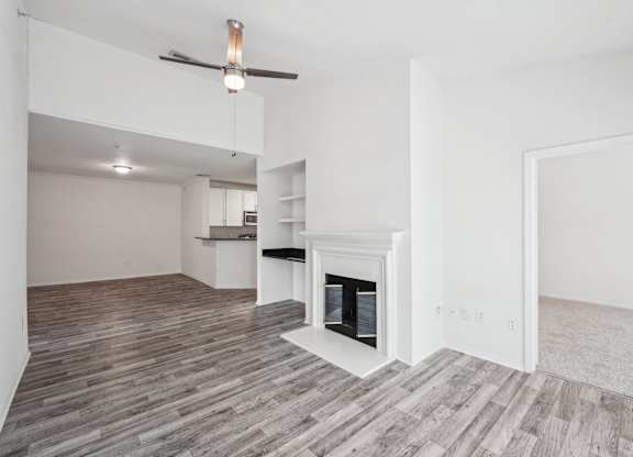 A living room with a fireplace, a ceiling fan, and shelving with a desk area.