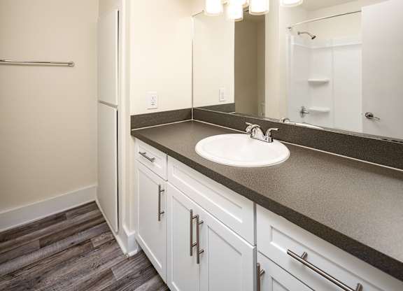 A bathroom with a sink, mirror, and wooden floors.